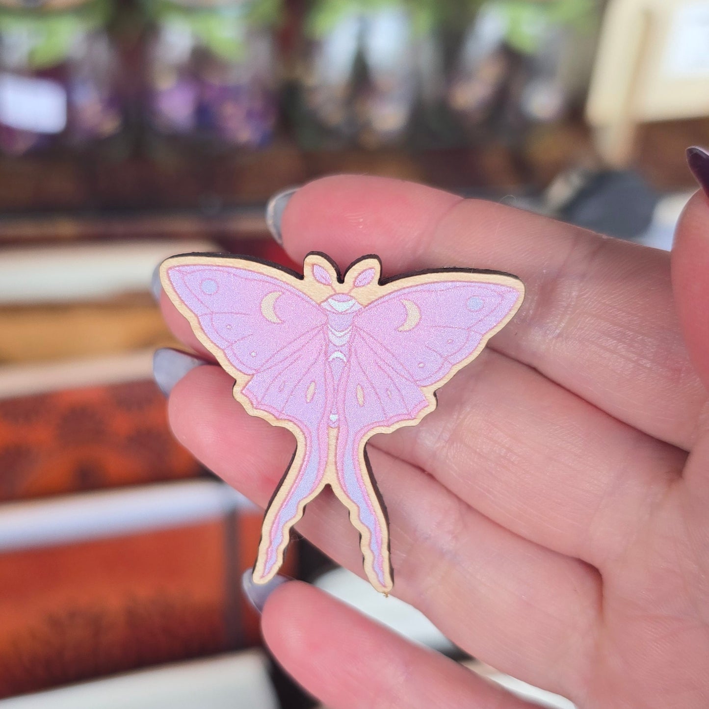 Hand holding a pink moth pin against a blurred store background